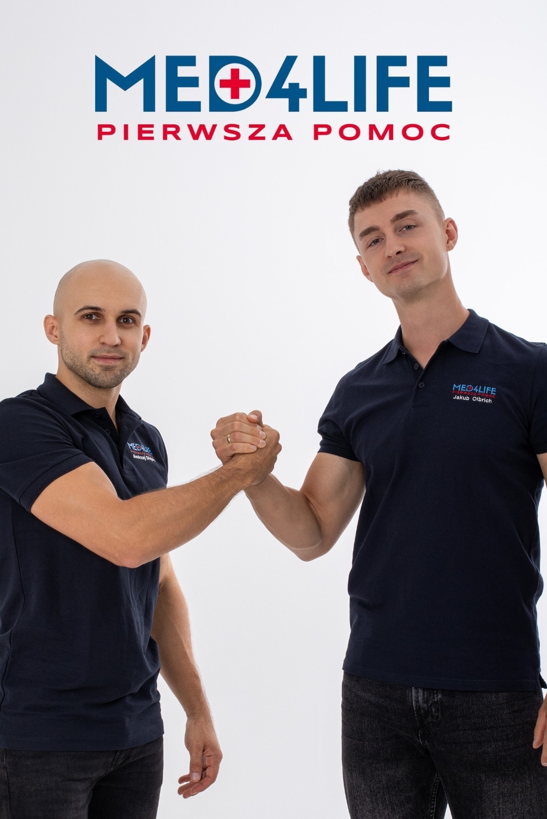 Dwóch mężczyzn w granatowych koszulkach polo z logo firmy Med4Life podaje sobie ręce na białym tle, symbolizując partnerstwo i gotowość do działania.