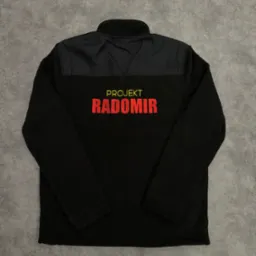 Czarna bluza polarowa z krótkim zamkiem, z nadrukiem 'Projekt Radomir' w kolorze czerwonym, leżąca na szarym tle.