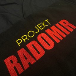 PIXEL HAFT - Czarna bluza z kontrastowym górnym panelem i wyhaftowanym napisem 'PROJEKT RADOMIR' w kolorach żółtym i czerwonym, widoczne detale ściegów.