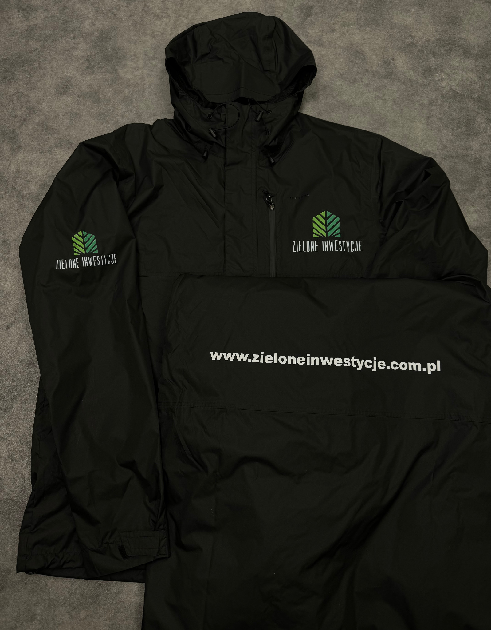 Czarna kurtka przeciwdeszczowa z kapturem, z nadrukowanym logo i nazwą firmy 'Zielone Inwestycje' oraz adresem strony internetowej, leżąca na szarym tle.