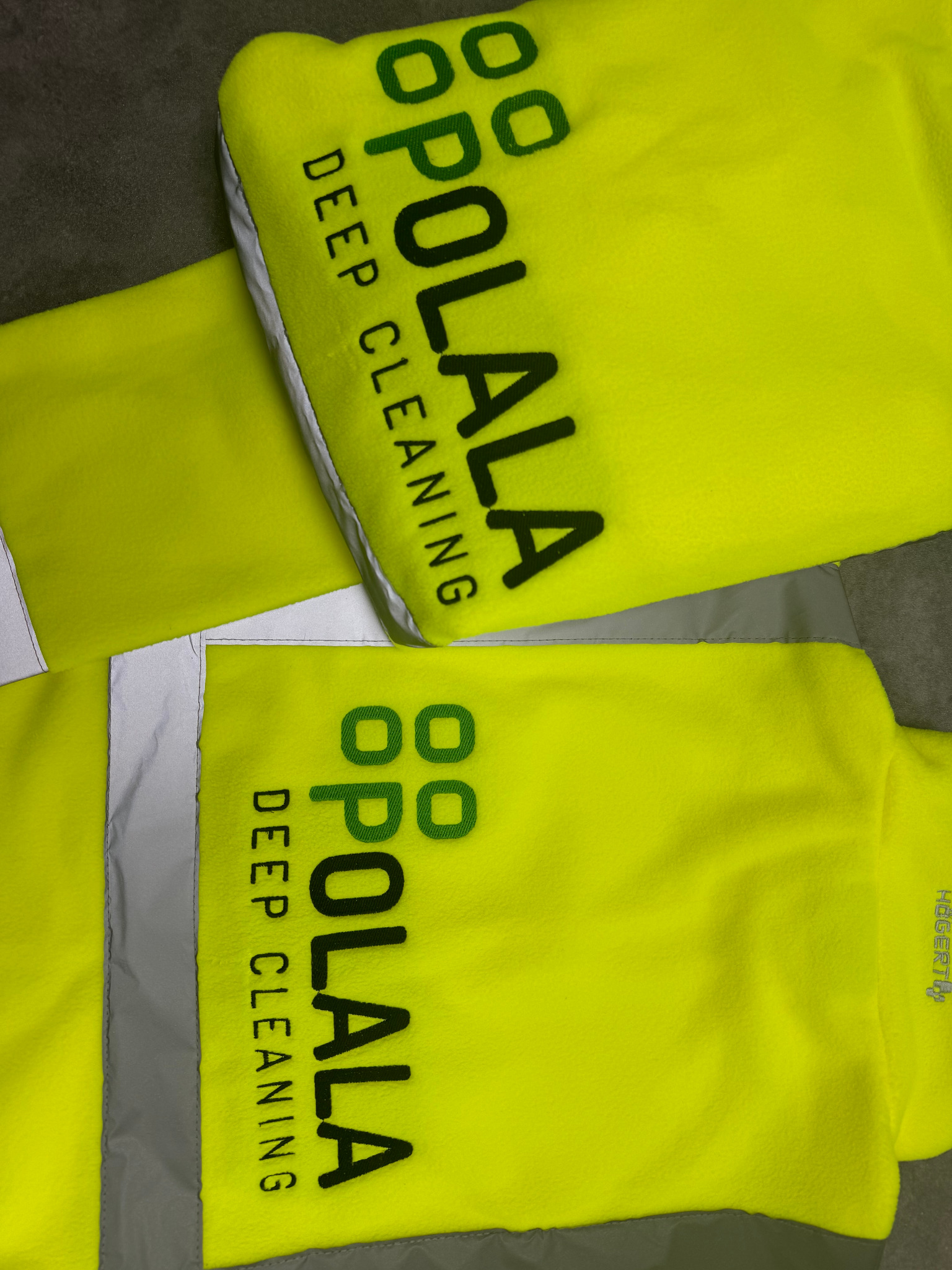 Dwa żółte, polarowe pokrowce na mopy parowe z nadrukowanym logo 'OPOLALA DEEP CLEANING' w kolorze czarnym i zielonym, widoczne szare obszycie i fragmenty szarej tkaniny.