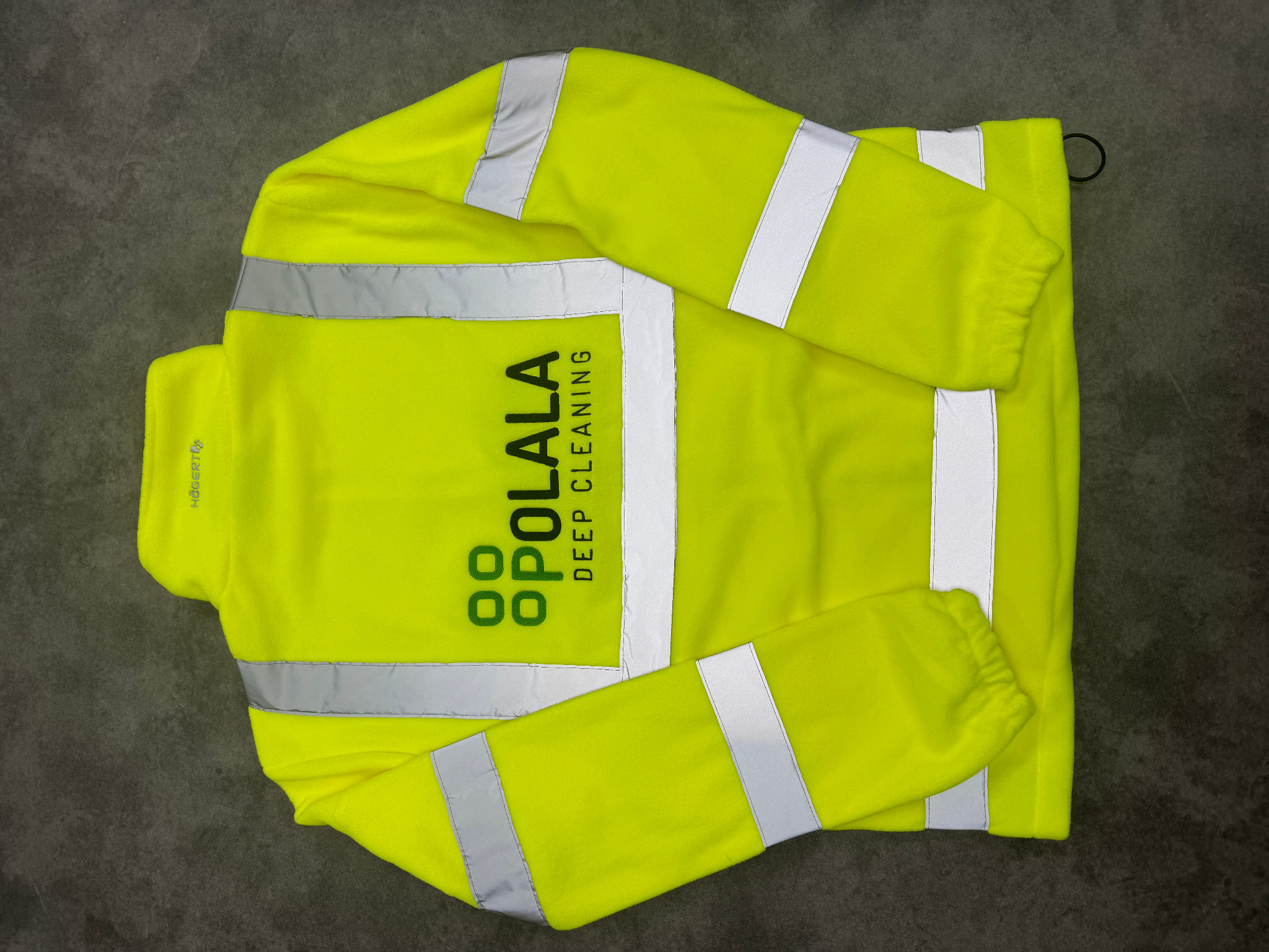 Rozłożona, jaskrawożółta bluza polarowa z odblaskowymi pasami i nadrukowanym logo 'POLALA DEEP CLEANING' na plecach, leżąca na szarym tle.