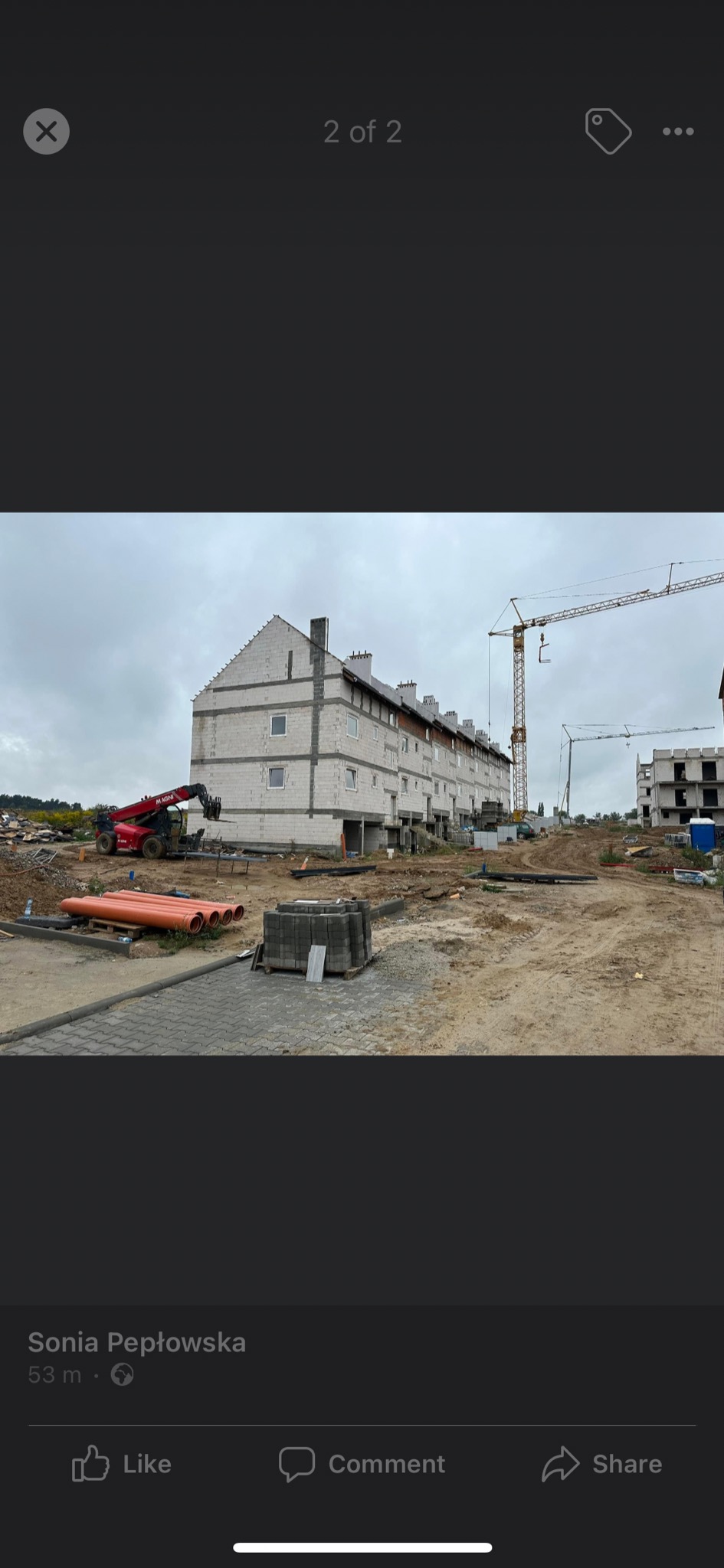 Budowa wielorodzinnego budynku z białych bloczków, widoczny dźwig budowlany i materiały budowlane na placu budowy.