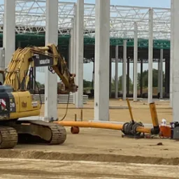 Żółta koparka Komatsu na placu budowy hali magazynowej, rury kanalizacyjne w wykopie ziemnym.