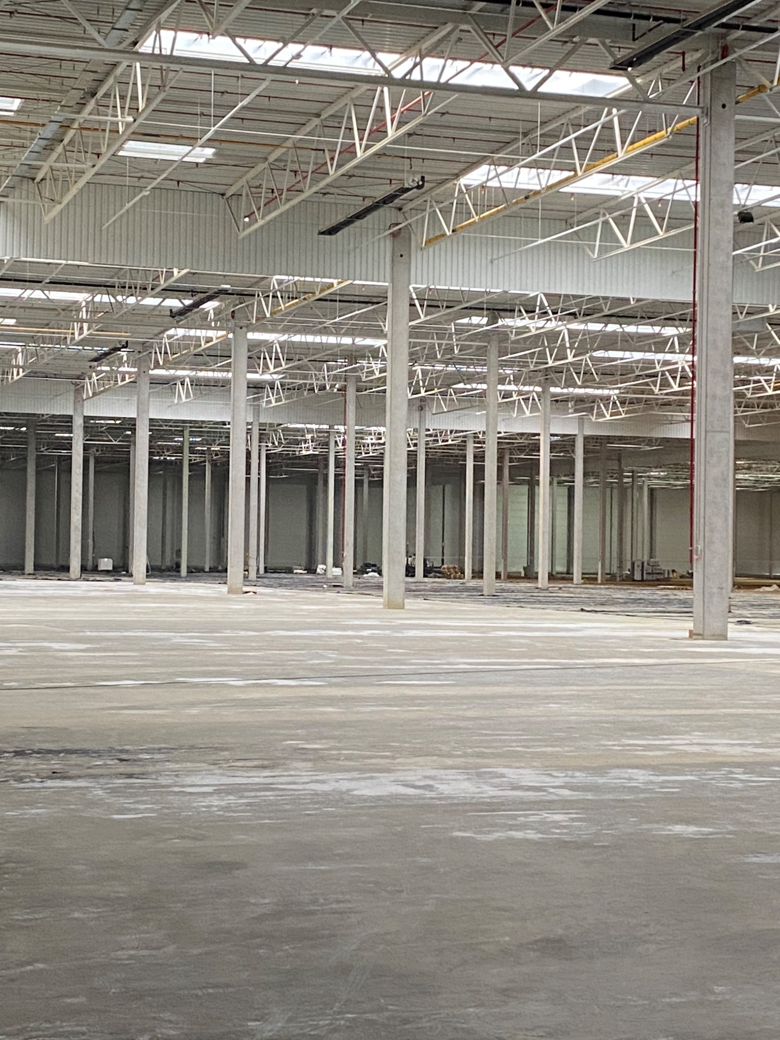Przestronne wnętrze pustego magazynu z betonową podłogą, metalową konstrukcją dachu i rzędami betonowych słupów.