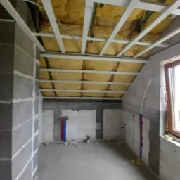 Poddasze w trakcie ocieplania wełną mineralną, widoczne profile stalowe, ściany z betonu komórkowego, instalacja wodna z rurami PEX.