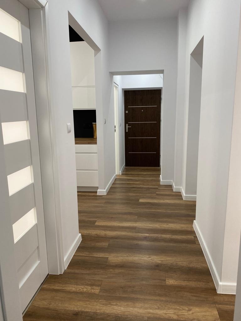 Korytarz po remoncie z nową, drewnopodobną podłogą z paneli, białymi ścianami i drzwiami, widok w głąb mieszkania.