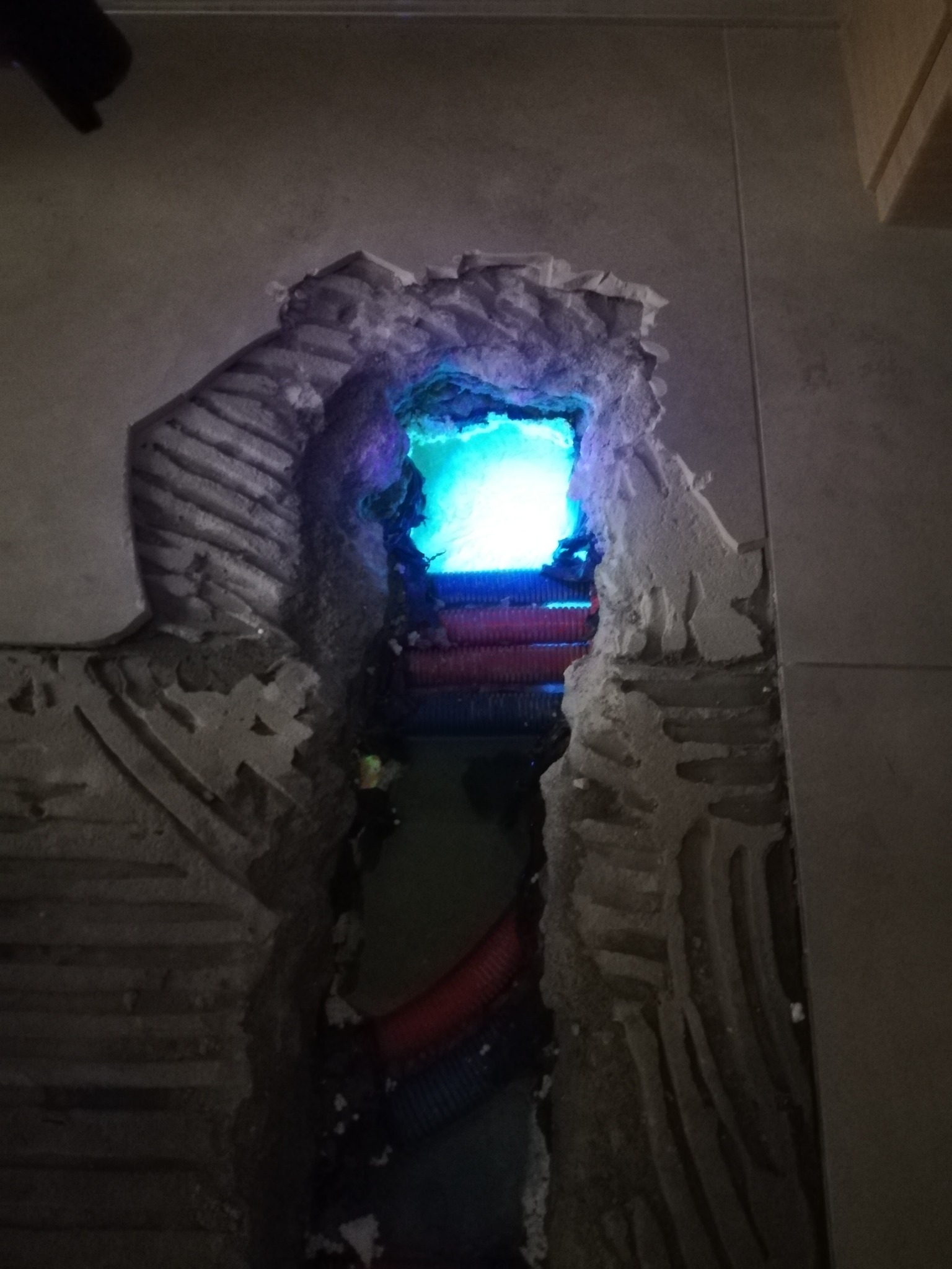 Wykuty otwór w ścianie z widocznymi rurami wewnątrz, podświetlonymi na niebiesko, ukazujący etap prac instalacyjnych.