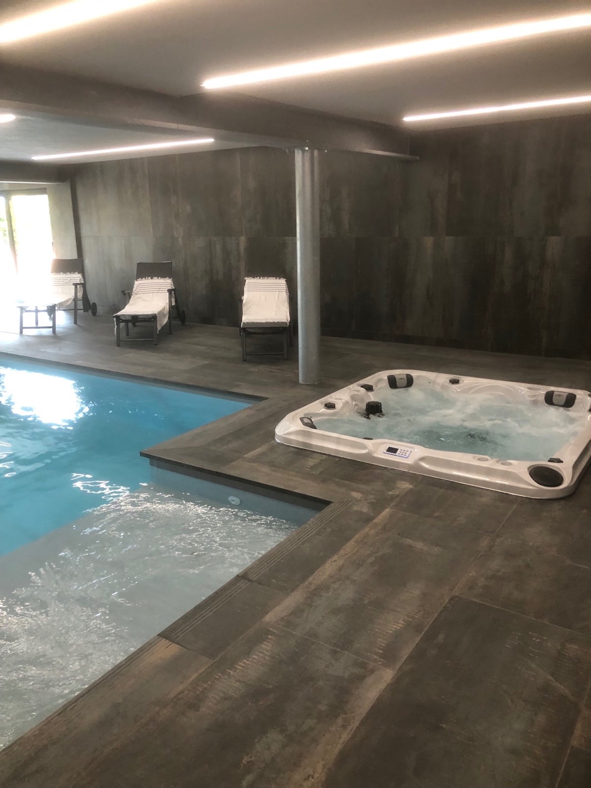 Wnętrze luksusowego basenu z jacuzzi w Katowicach, wykończone ciemnymi płytkami imitującymi beton, z trzema leżakami ustawionymi przy ścianie.