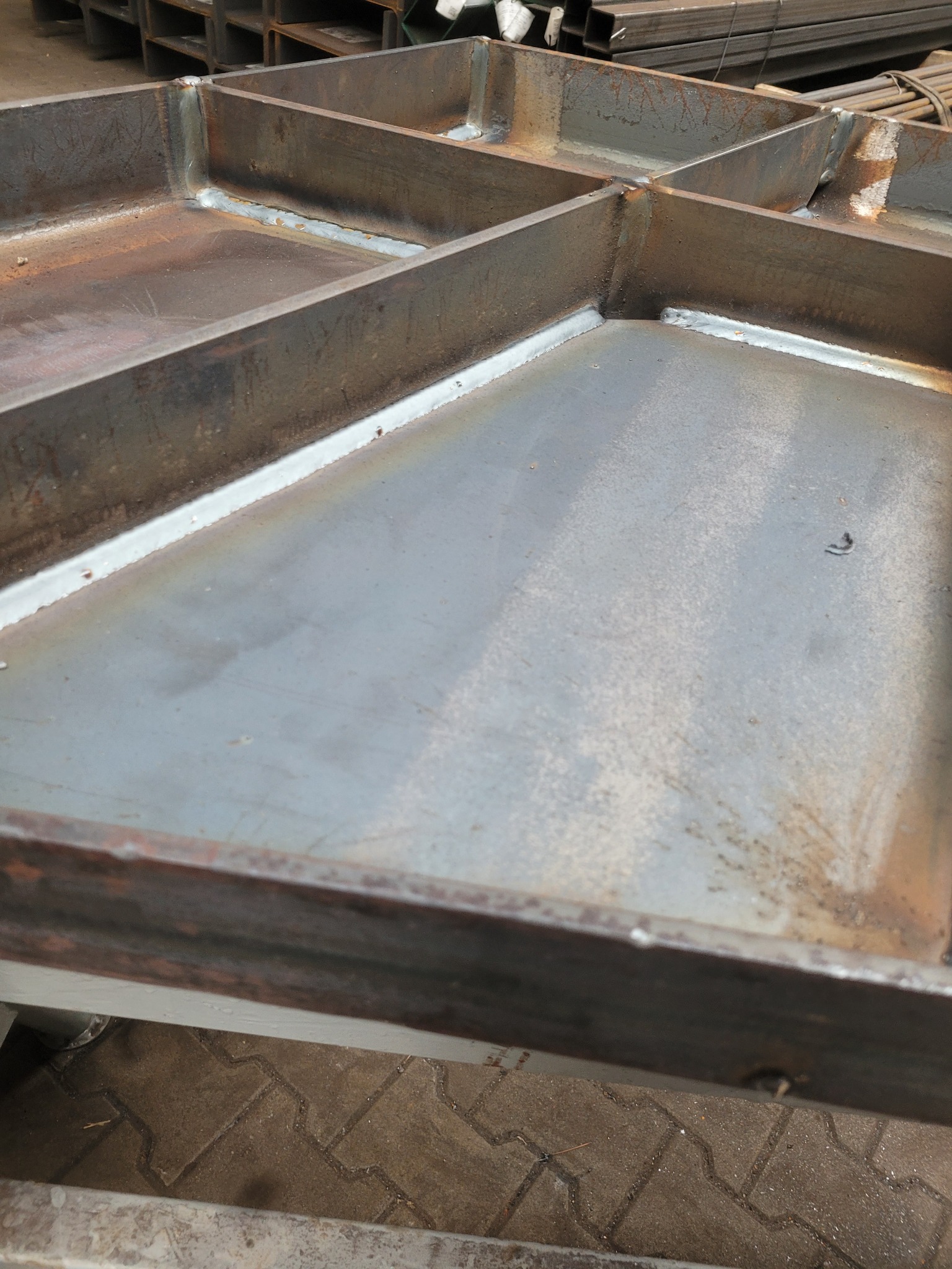 Metalowa konstrukcja kratowa z widocznymi spawami, surowy stan przed obróbką, w tle profile stalowe.