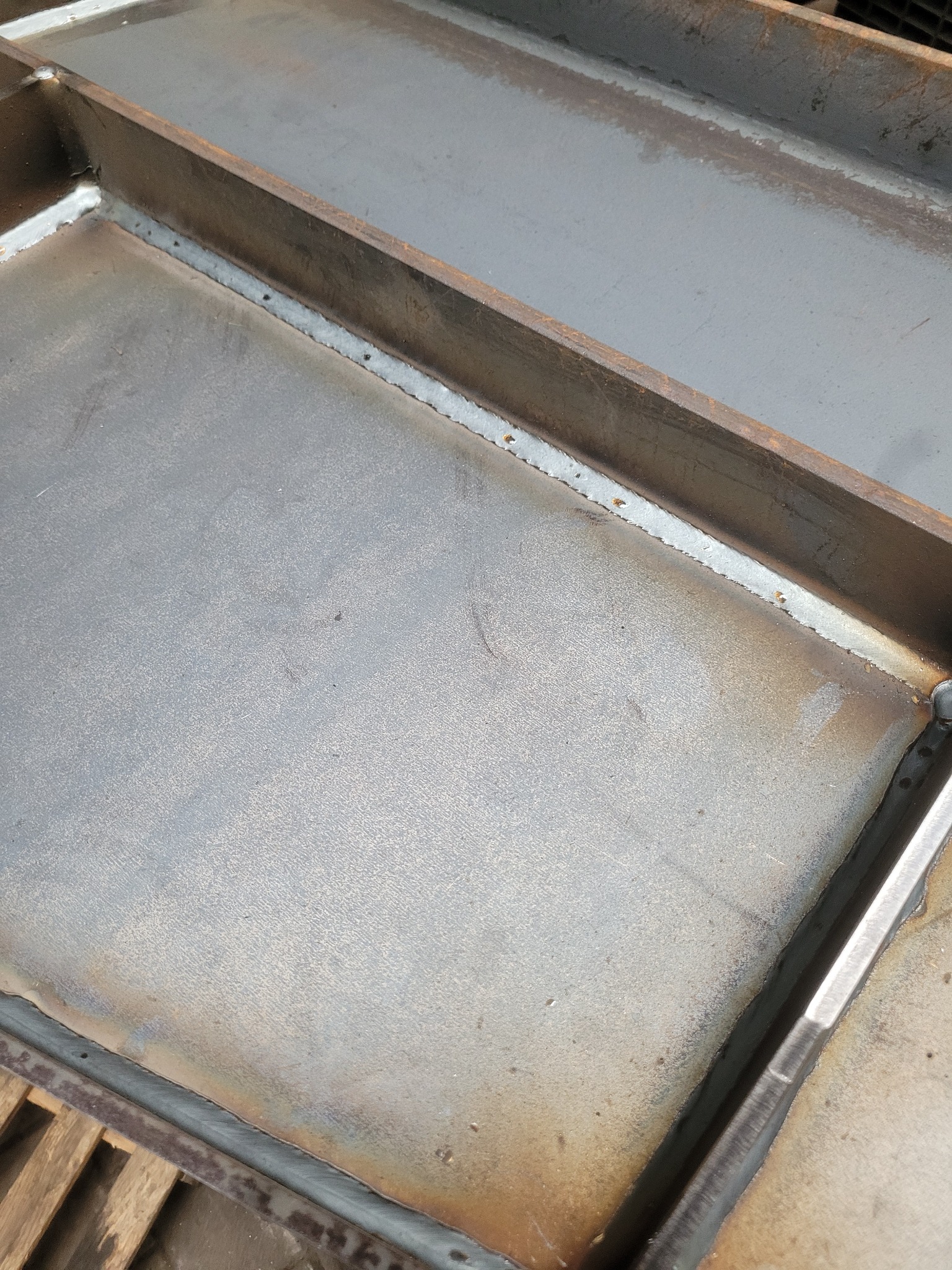 Fragment stalowej konstrukcji z widocznymi spawami, ukazujący proces łączenia elementów pod kątem, z lekkimi przebarwieniami termicznymi na powierzchni metalu.