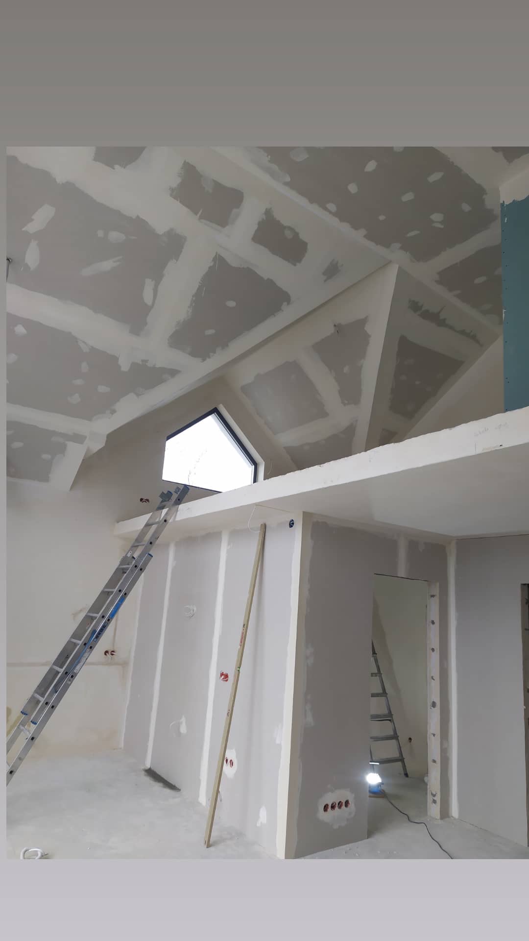 Skośny sufit na poddaszu z zamontowaną płytą kartonowo-gipsową, widoczne łączenia płyt wymagające szpachlowania, drabina oparta o ścianę z trójkątnym oknem.