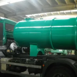 Zielony samochód ciężarowy z cysterną, świeżo po malowaniu, widoczny w hali warsztatowej. Błyszcząca powierzchnia zbiornika, oświetlenie hali.