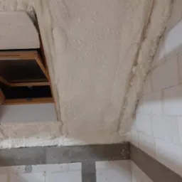 Poddasze z oknem dachowym po natrysku pianki izolacyjnej, widoczne białe bloki konstrukcyjne i elementy betonowe.