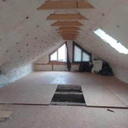 Usługi Budowlane Sylwester Zinko - Poddasze po ociepleniu pianką PUR z widoczną drewnianą konstrukcją dachu i oknami dachowymi, częściowo wyłożone płytami OSB z otworem rewizyjnym.