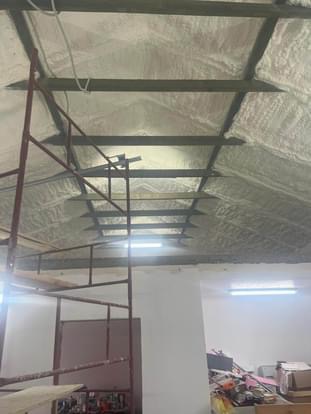 Poddasze z widoczną konstrukcją dachu pokrytą białą pianą izolacyjną, rusztowanie w lewym rogu, widoczne oświetlenie LED.