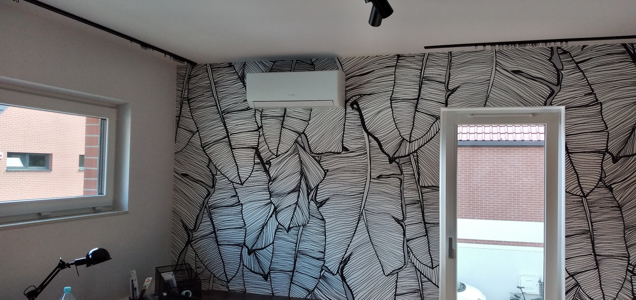 Biały klimatyzator ścienny zamontowany na ścianie z tapetą w motywie liści bananowca w nowoczesnym wnętrzu domu.