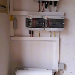 HELIOLINE - Biały magazyn energii Huawei obok białej ściany z zamontowanym inwerterem i rozdzielnicami elektrycznymi.