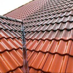 HELIOLINE - Częściowo umyty, mokry dach z czerwonej dachówki ceramicznej. Widoczny kontrast czystej i zabrudzonej powierzchni. Woda spływa po powierzchni dachu.