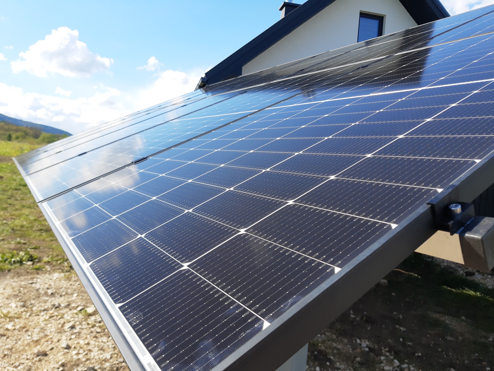 Instalacja fotowoltaiczna na dachu domu jednorodzinnego z widocznym krajobrazem w tle, w słoneczny dzień.