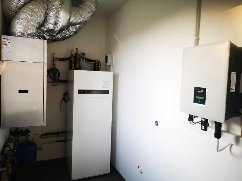 Białe jednostki pompy ciepła i falownik zamontowane w pomieszczeniu z widocznymi rurami i instalacją.