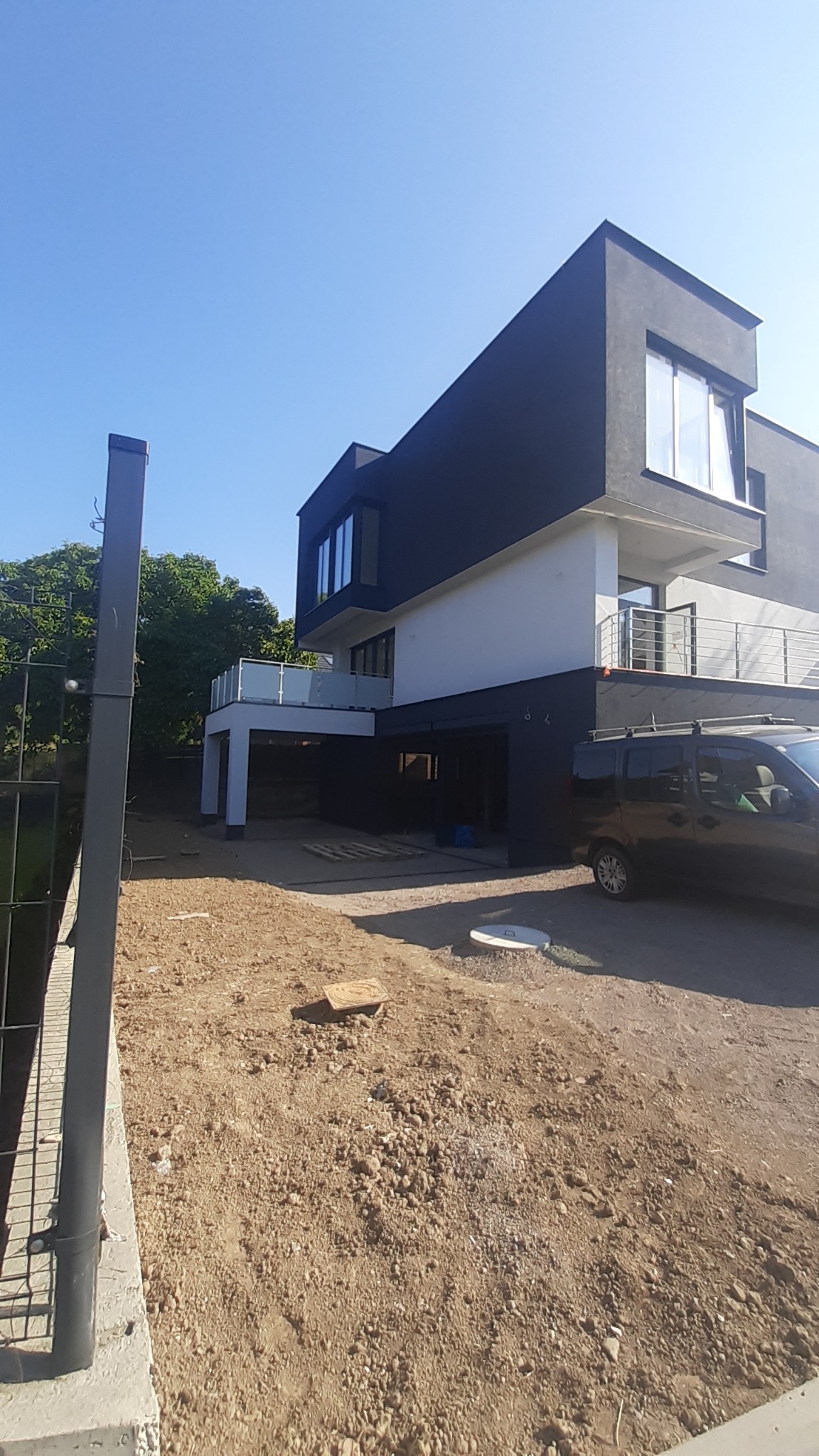 Nowoczesny dom z czarno-białą elewacją, widok z zewnątrz na fragment terenu przed domem i zaparkowany samochód dostawczy