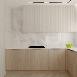 Sylwia Serwa Architekt Wnętrz - Minimalistyczna kuchnia z drewnianymi szafkami, marmurowym blatem i ścianą, czarną płytą grzewczą oraz owocami w szklanej misie.