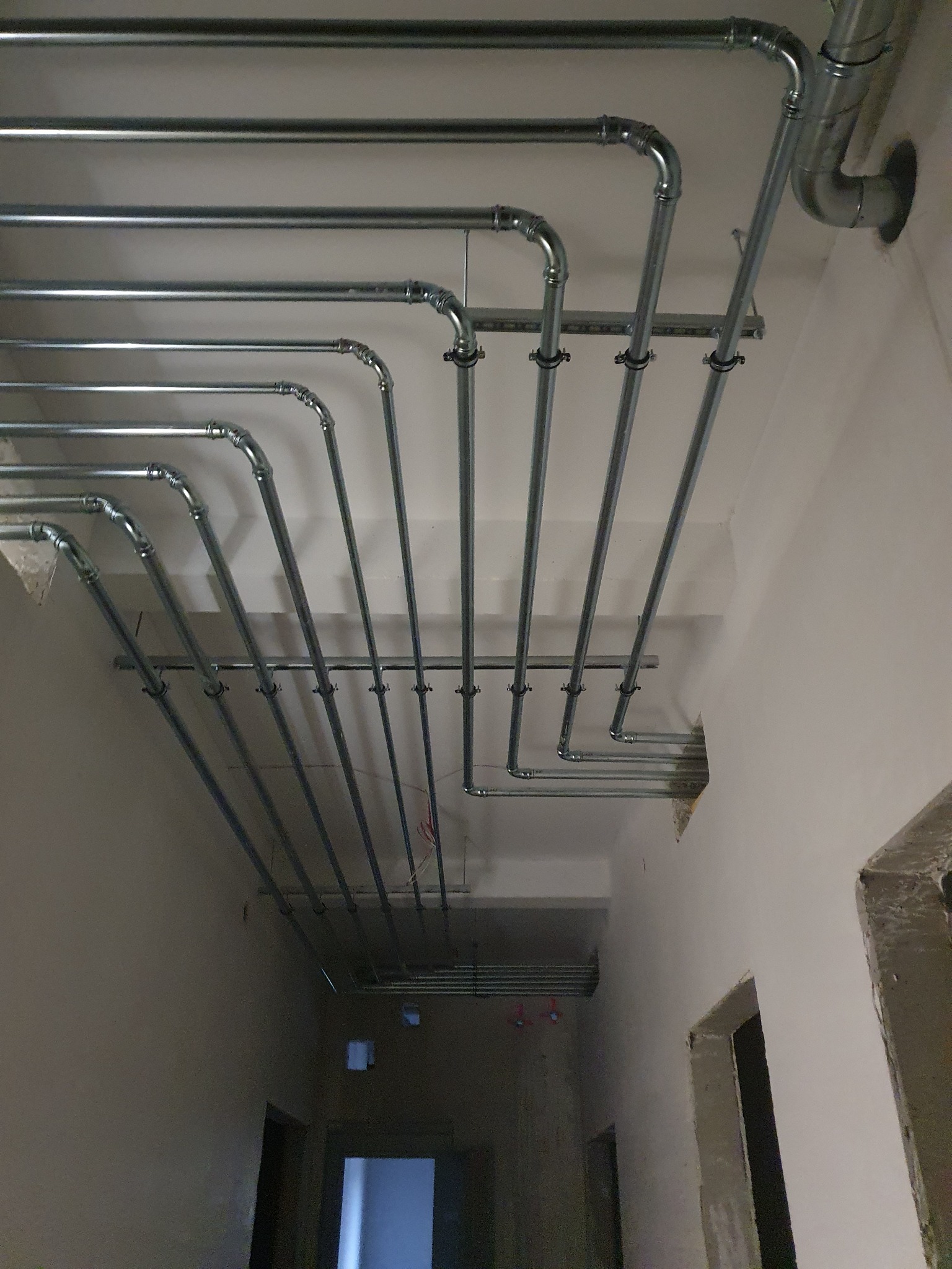 Równoległe rury instalacyjne, zamocowane do sufitu w budynku w Krakowie, z widocznymi złączkami i mocowaniami.
