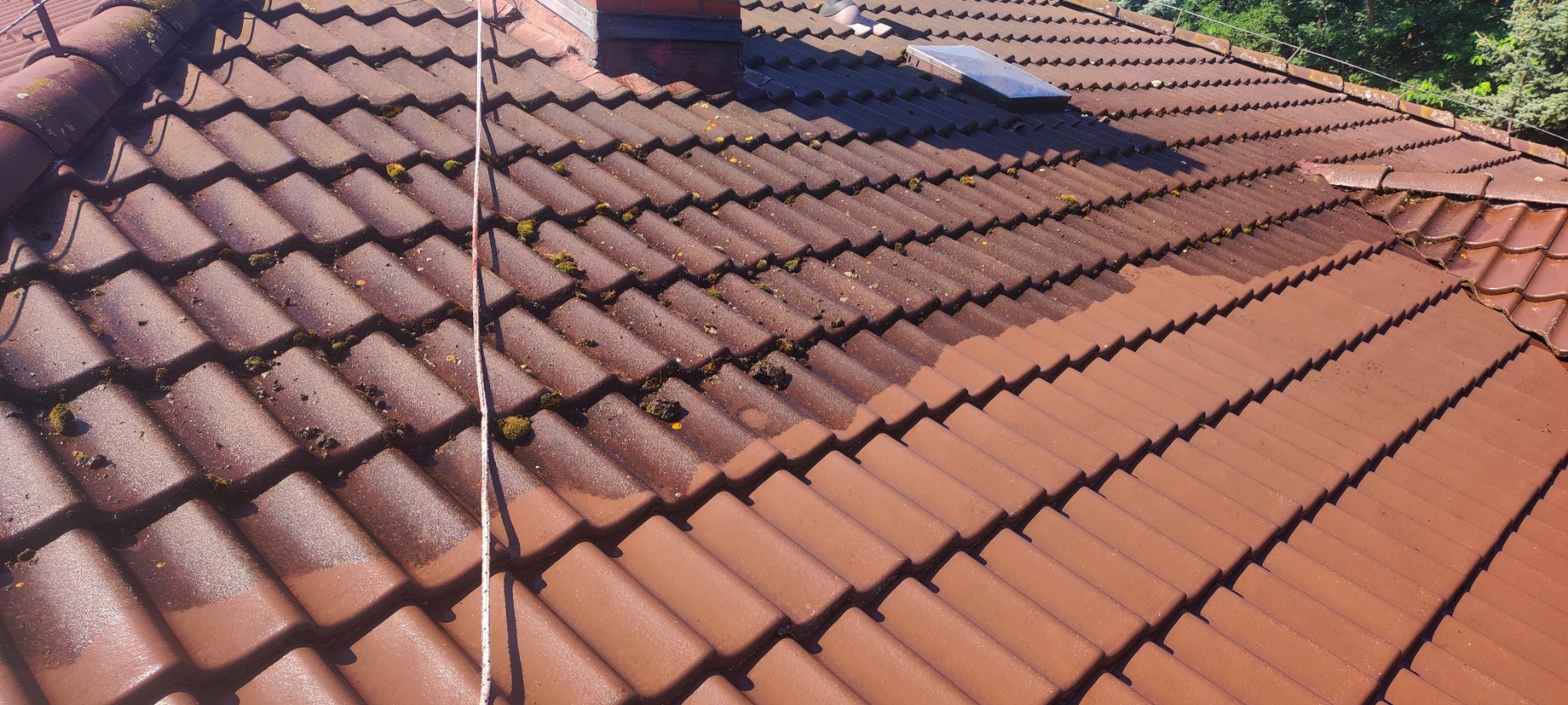 Czyszczona dachówka ceramiczna, widoczny kontrast między umytą a zabrudzoną częścią dachu, z mchem i zabrudzeniami organicznymi.