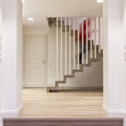 Dom Pracy Twórczej Łukasz Engel - Wnętrze domu w Cyganówce z drewnianymi schodami wspornikowymi i osobą w czerwonej bluzce wchodzącą na górę, widoczne z dołu schodów.