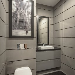 Dom Pracy Twórczej Łukasz Engel - Nowoczesna łazienka w odcieniach szarości z poziomymi płytkami, wiszącą toaletą, szafką z umywalką i czarnym dywanikiem; na ścianie wisi oprawiona w ramę fotografia Angkor Wat.