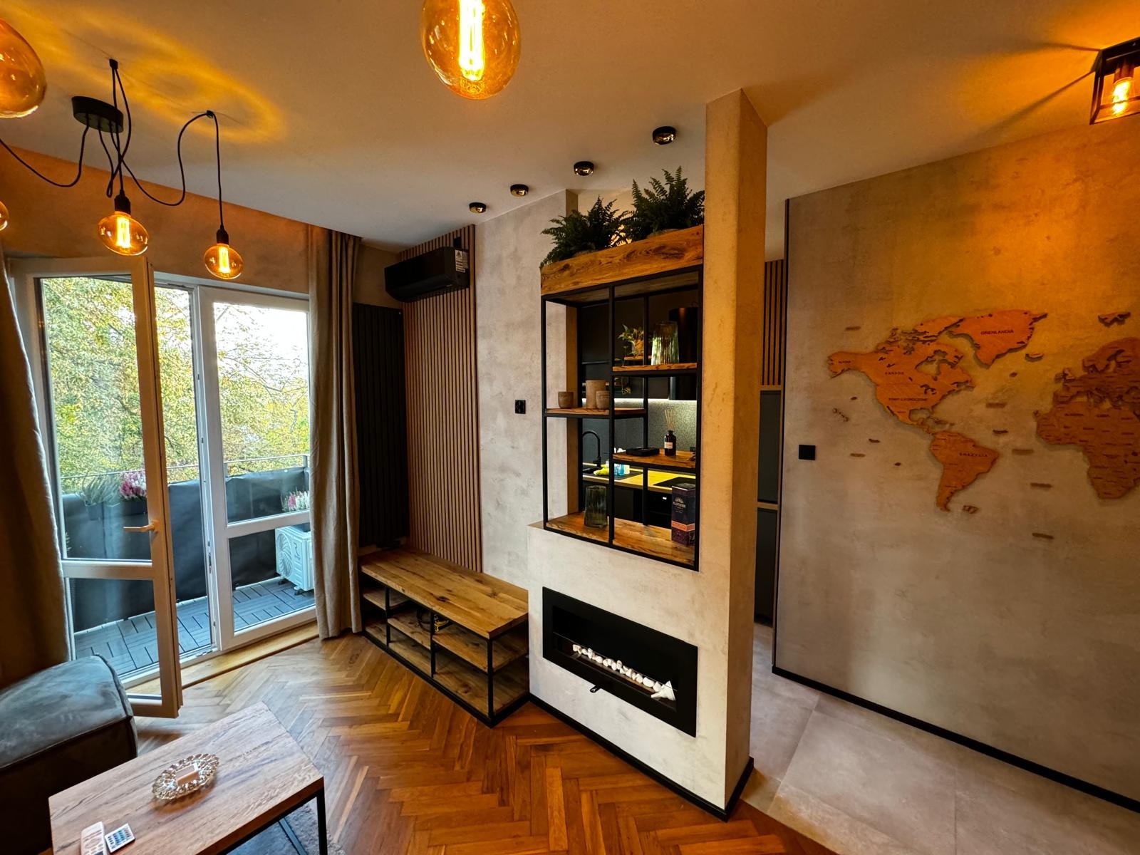 Nowoczesny salon z drewnianą podłogą w jodełkę, ścianą z mapą świata i półką regałową z roślinami nad kominkiem.