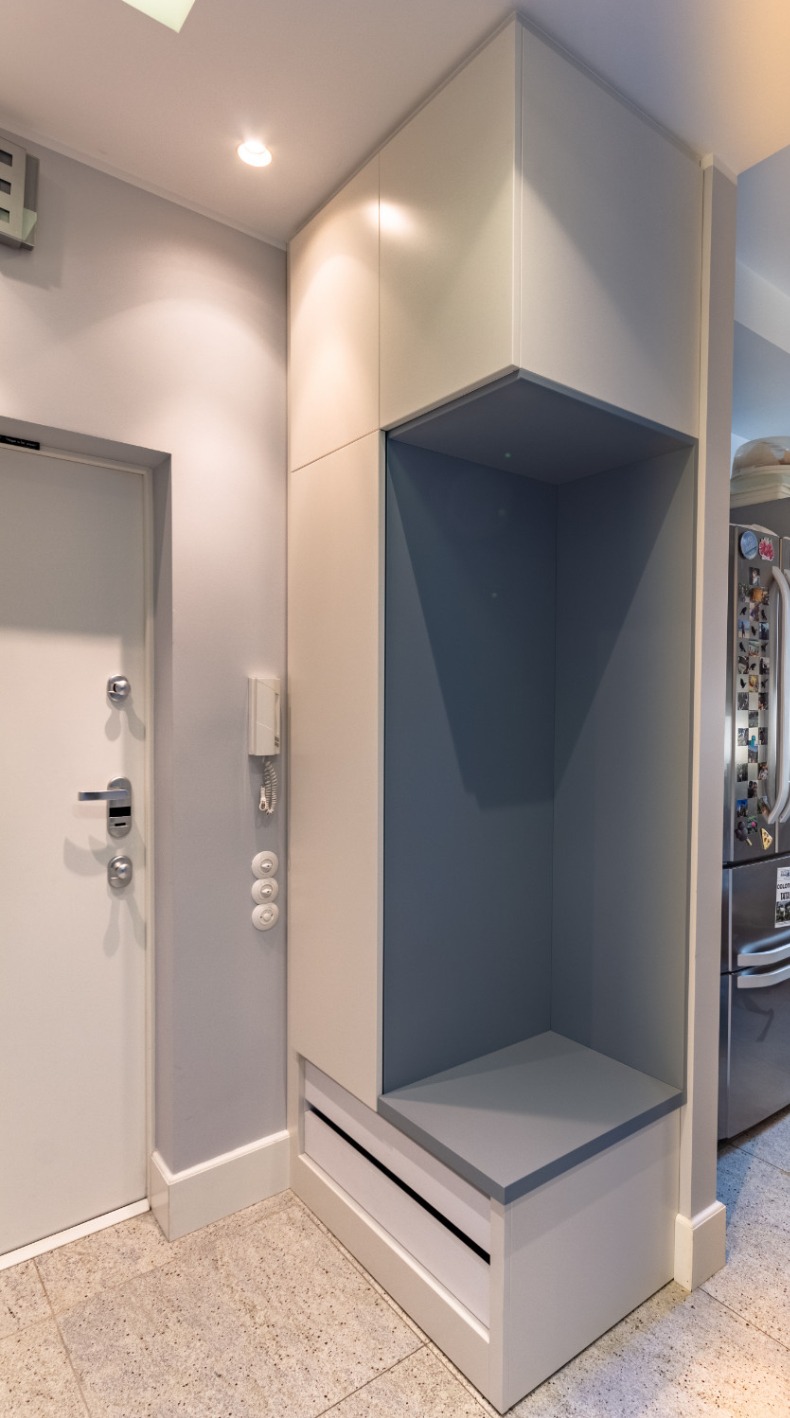 Nowoczesna szafa wnękowa w przedpokoju, z otwartą półką w kolorze gołębim i szufladami na dole, obok drzwi wejściowych i domofonu.