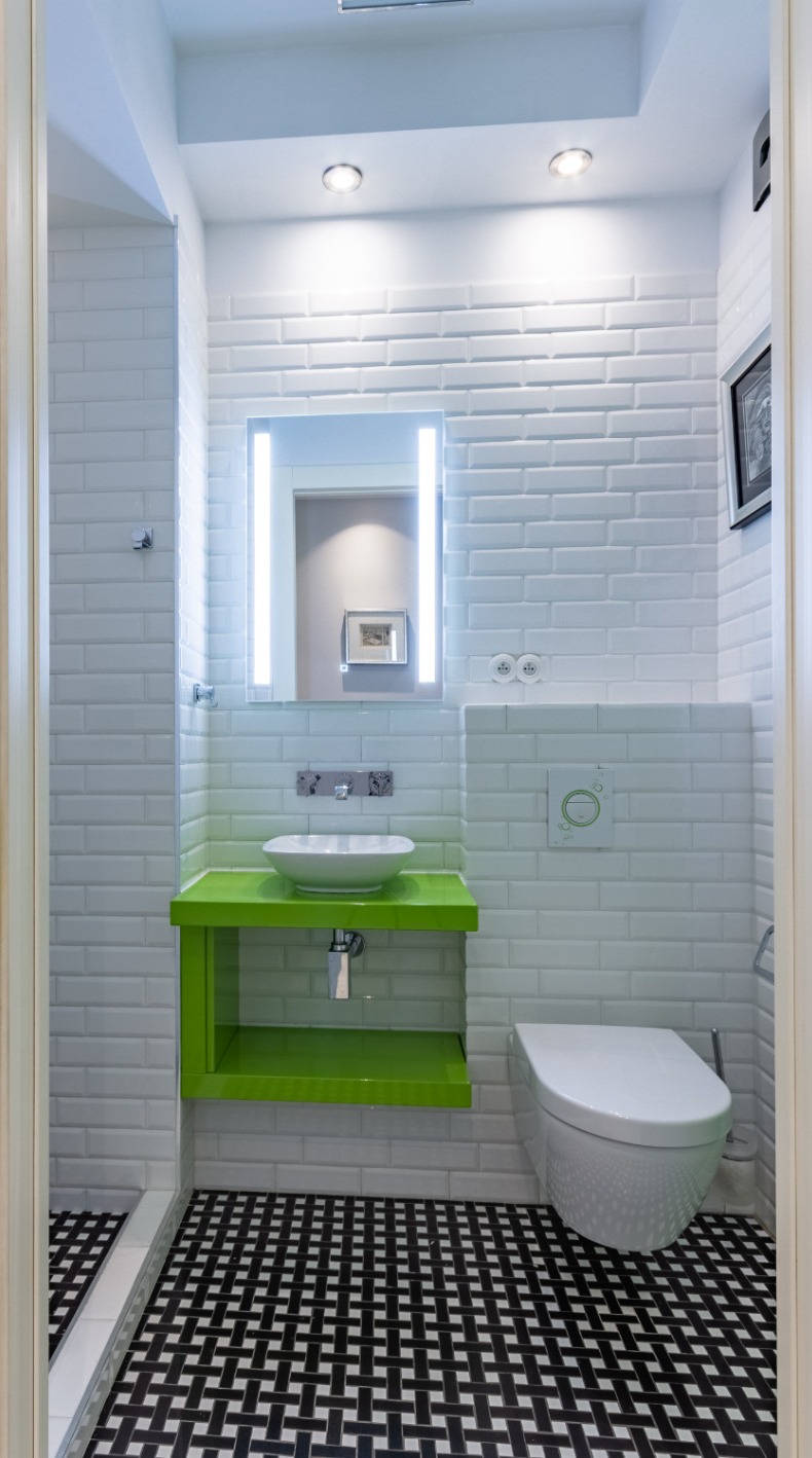Nowoczesna łazienka z białymi cegiełkami na ścianach, umywalką na zielonym blacie, podświetlanym lustrem i czarno-białą podłogą w geometryczny wzór.