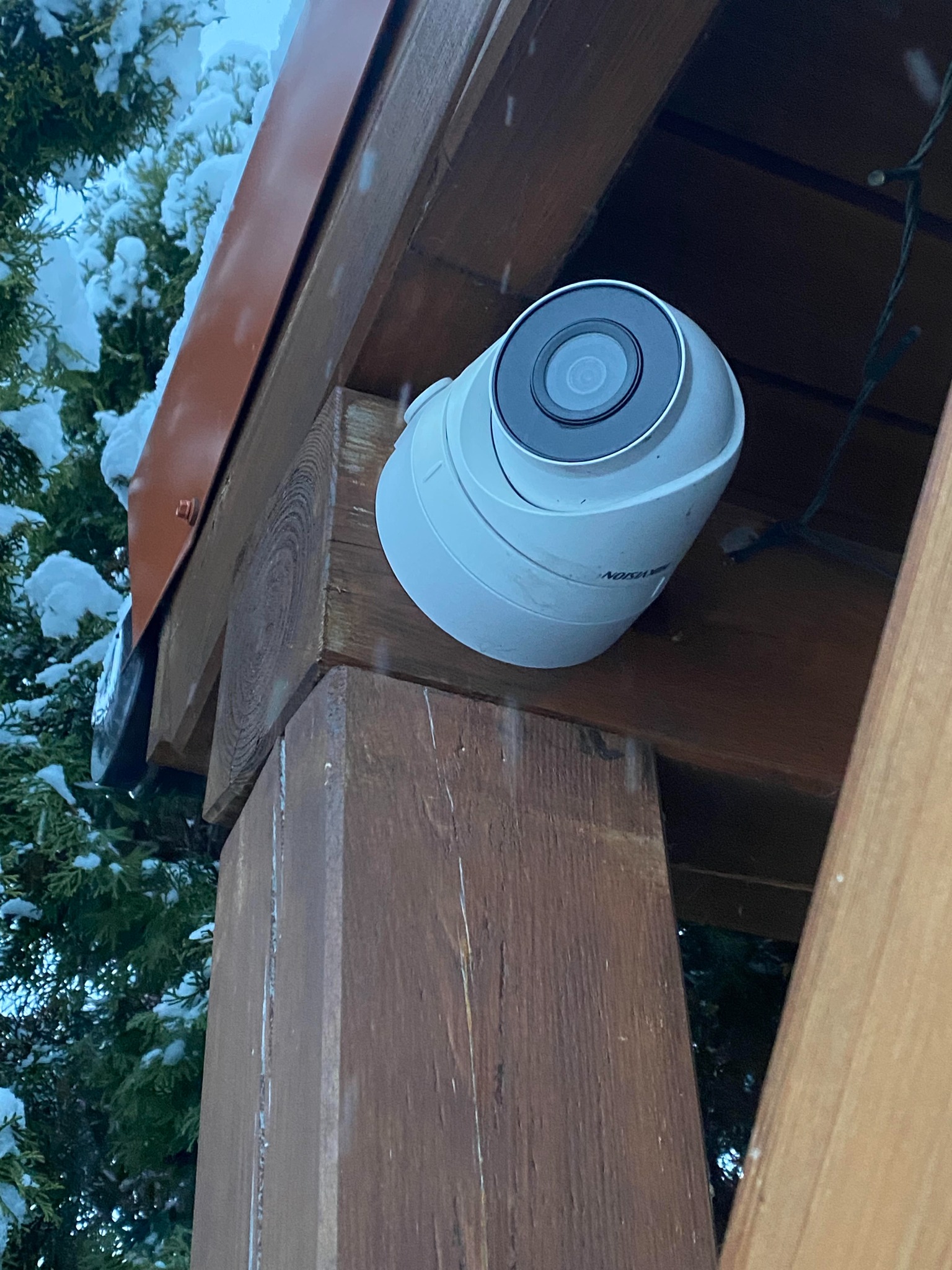 Kamera kopułkowa marki Hikvision zamontowana na drewnianej konstrukcji z widocznym śniegiem na tle iglaków.