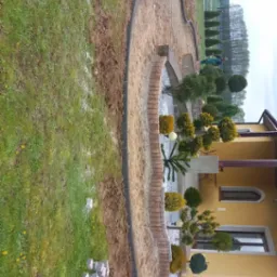 Kształtowanie terenu pod ogród z obrzeżami z kostki i przygotowaną podbudową, widoczne kostki do ułożenia na trawniku, w tle żółty budynek.