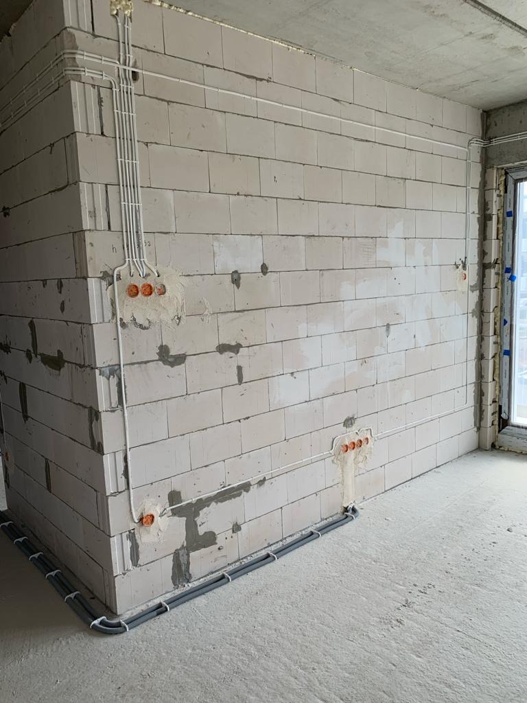 Surowe ściany z betonu komórkowego z widocznymi przewodami elektrycznymi w peszlach i puszkami instalacyjnymi, w trakcie montażu instalacji elektrycznej.