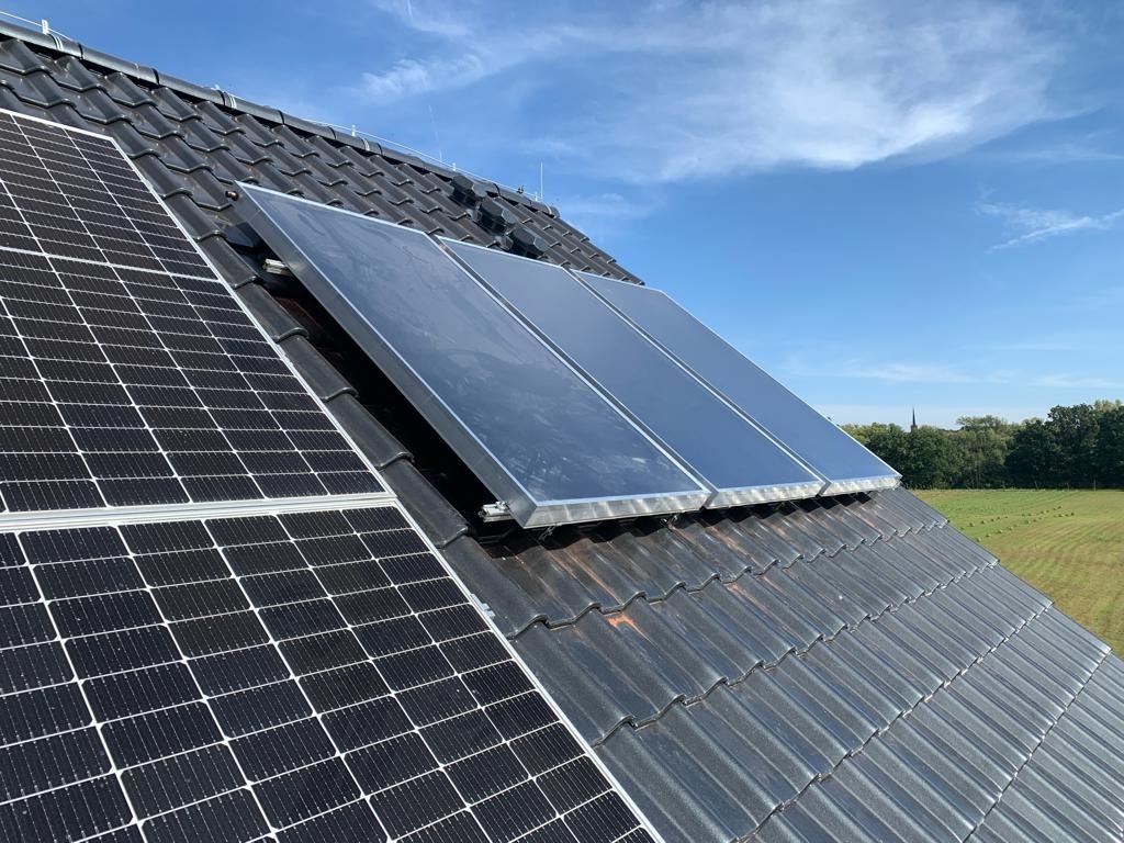 Panele słoneczne i kolektory słoneczne zamontowane na skośnym dachu pokrytym ciemną dachówką, widok z dołu w słoneczny dzień.