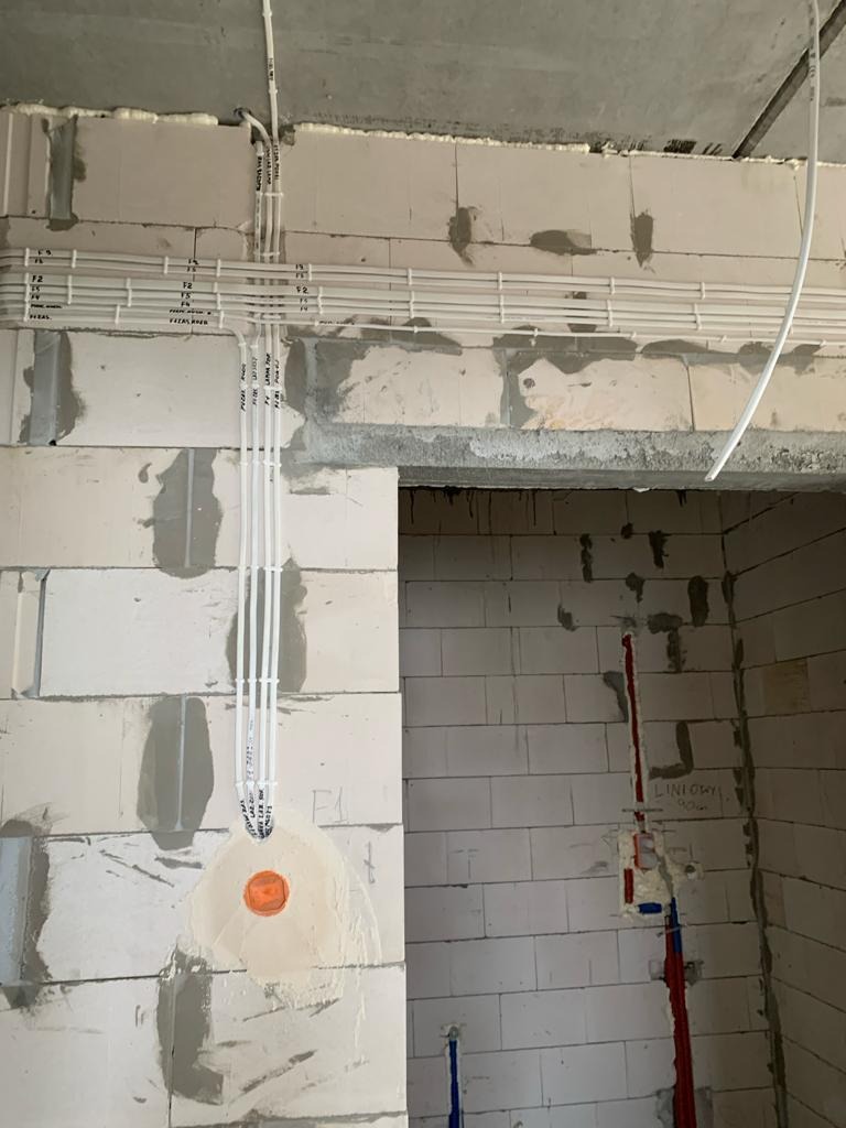 Białe rurki instalacyjne prowadzone po surowych ścianach z betonu komórkowego, widoczne otwory pod gniazdka i przewody, instalacja w trakcie realizacji.