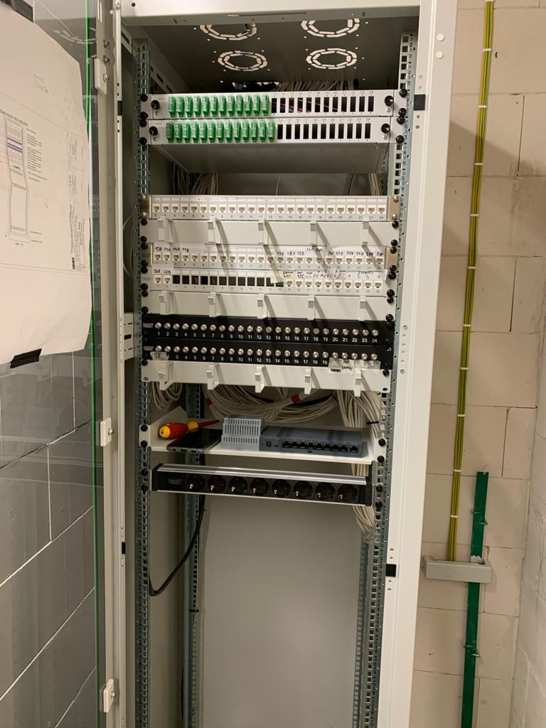 Otwarta szafa rackowa z panelami krosowniczymi, listwą zasilającą i okablowaniem, widoczne przewody poprowadzone wzdłuż ściany.