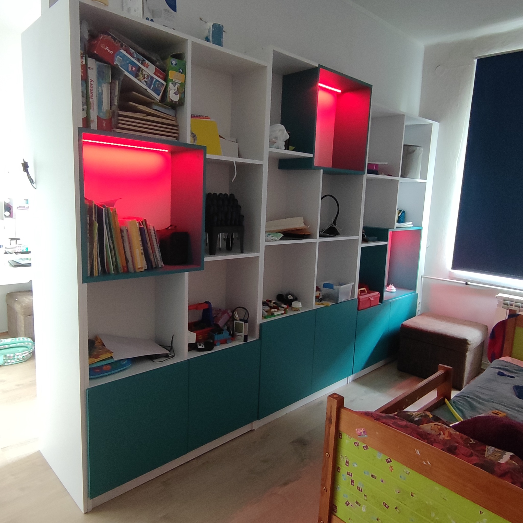 Biało-turkusowa szafa z otwartymi półkami, podświetlona czerwonymi listwami LED w pokoju dziecięcym.