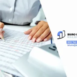 Kobieta w jasnej koszuli zaznacza ołówkiem dane w tabeli z kalkulatorem obok, na tle logo biura rachunkowego Małgorzata Górska.