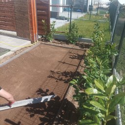 DaMaR Usługi koparką - Ręczne wyrównywanie ziemi pod trawnik z rolki, widoczne obrzeża i sadzonki wzdłuż ogrodzenia. Praca w słoneczny dzień.