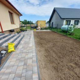 DaMaR Usługi koparką - Przygotowany teren pod trawnik z rolki, obok ułożona kostka brukowa z widocznymi schodami i workiem ziemi. W tle domy i ogrodzenie.