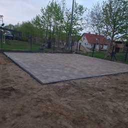 Koparka i Kostka -prace ziemne Koszalin - Ułożona kostka brukowa na posesji, widok z góry. Brązowo-szara kostka tworzy równą powierzchnię, obrzeża wykończone czarnym elementem. W tle domy i zieleń.