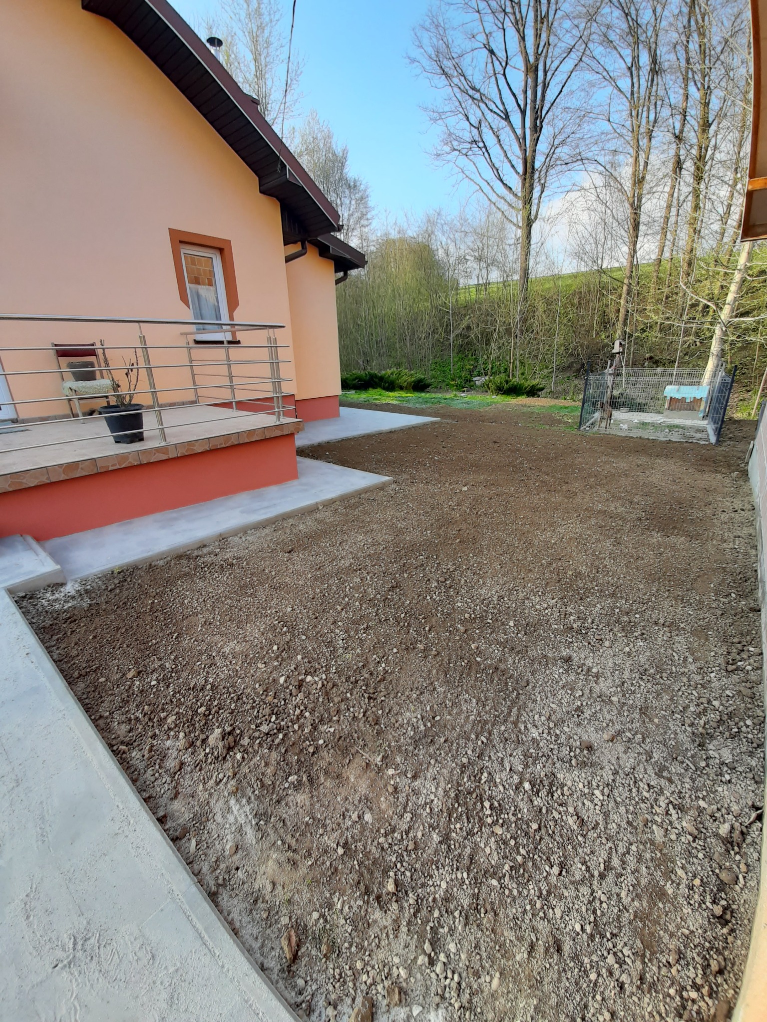 Przygotowany teren pod trawnik przy domu z pomarańczową elewacją, widoczne świeżo wylane betonowe obrzeża.
