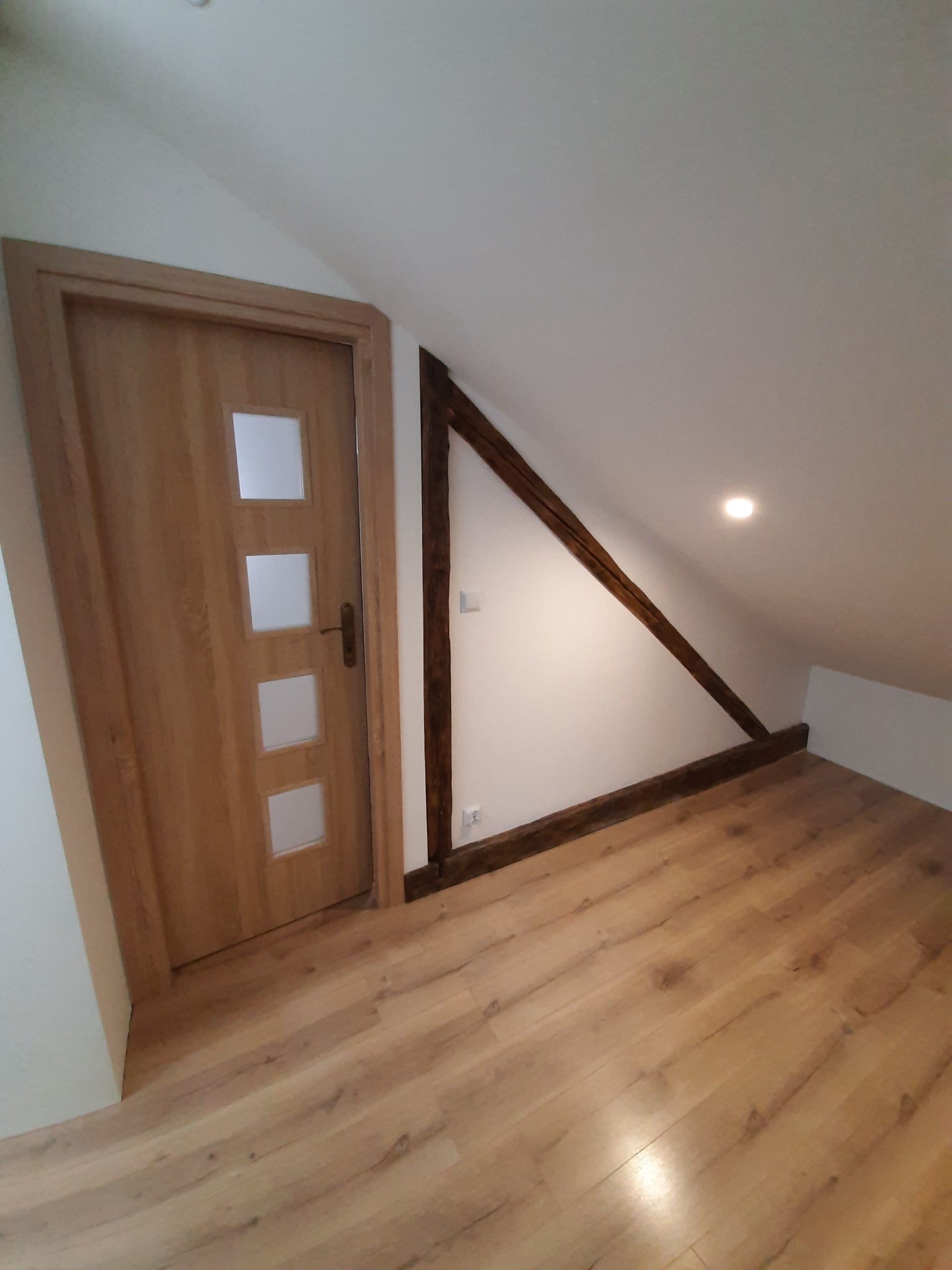 Gotowe poddasze z drewnianą podłogą, drewnianą ramą konstrukcyjną i nową, drewnianą, przeszkloną wewnętrzną stolarką drzwiową.