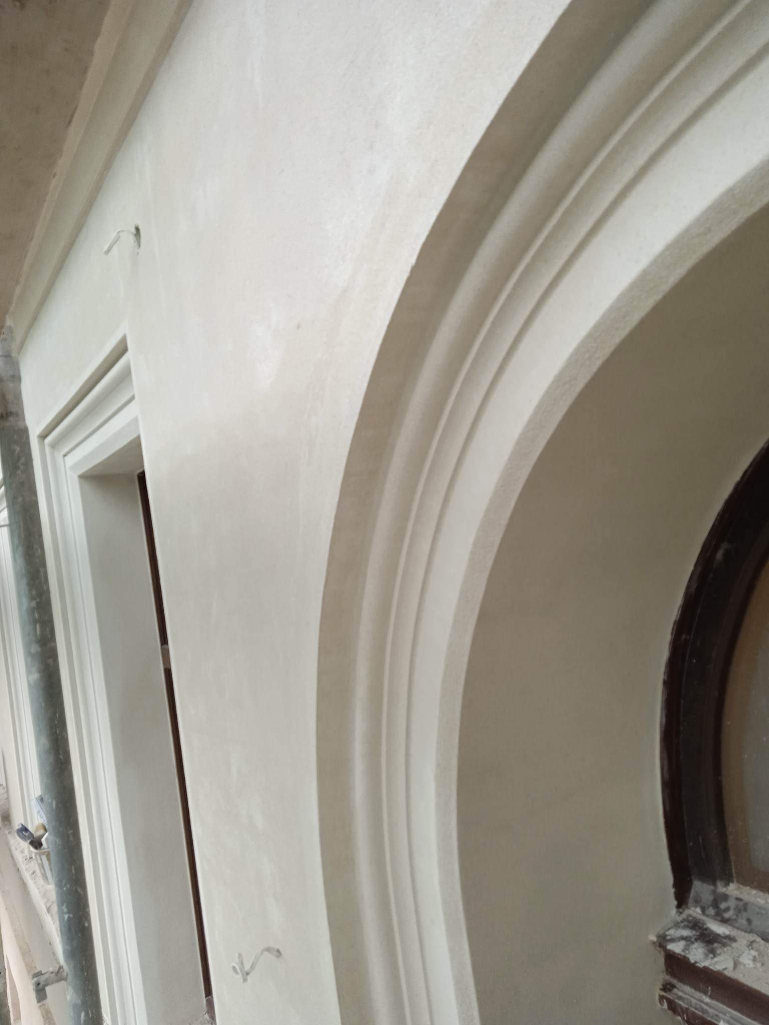Świeżo otynkowana, jasna elewacja z dekoracyjnymi łukami i sztukaterią w Poznaniu, widok z bliska na detale architektoniczne.