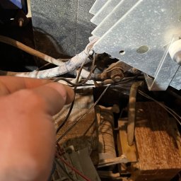 Mr-Elektro Kamil Janas - Wnętrze starego, zakurzonego urządzenia elektrycznego z widocznymi przewodami, płytką drukowaną i radiatorem, palec wskazujący na jeden z przewodów.