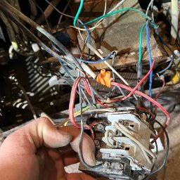 Mr-Elektro Kamil Janas - Brudny stycznik elektryczny trzymany w dłoni na tle splątanych przewodów i kabli. Widoczny pomarańczowy konektor. Na podłodze leży śrubokręt z czerwoną rękojeścią. Zdjęcie wykonane przed naprawą.